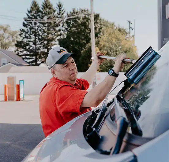 Daigle employee squeegeeing his van windshield in a gas station parking lot