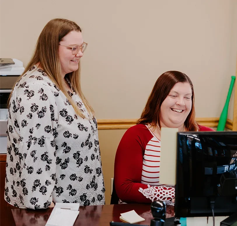 two woman smiling while looking at a computer