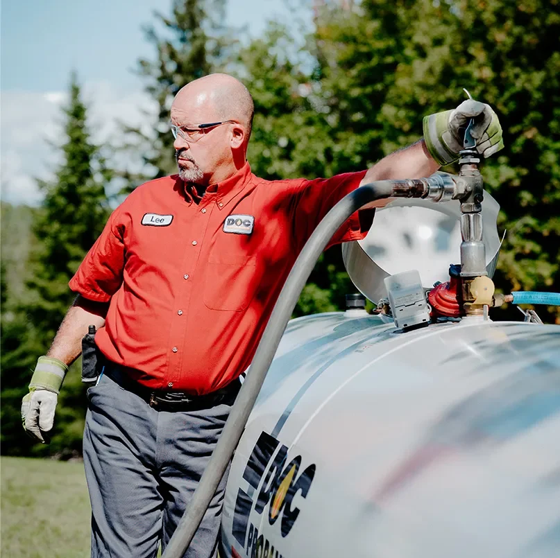 daigle employee filling a propane tank in a large field surrounded by pine trees
