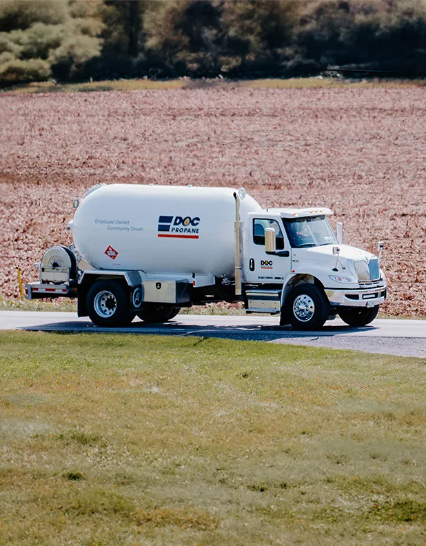 fuel truck traveling down a small rural road next to farmland