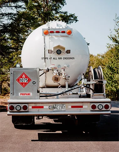 the rear of a Daigle propane delivery truck in a driveway surrounded by bushes