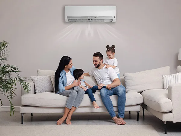 parents and two children sit in a modern white room below a min-split AC unit smiling at each other