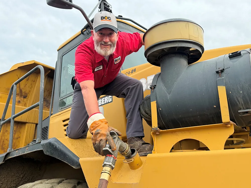 daigle employee hanging off an industrial dump truck connecting a hose