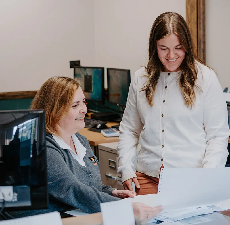 two daigle office workers smiling while looking at paperwork in the office