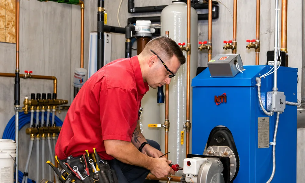 man in safety glasses and a work belt performing maintenance on a heating system