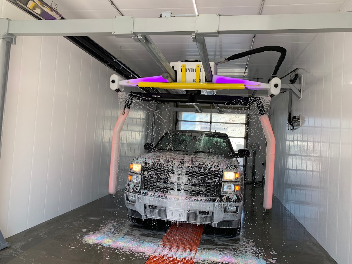 large truck driving covered in soap while driving through a clean white car wash