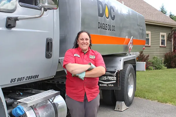 truck driver in her Daigle uniform stands next to her truck outside a residence.