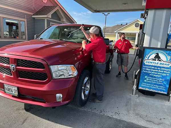 station employees washing a large red truck at a gas station pump