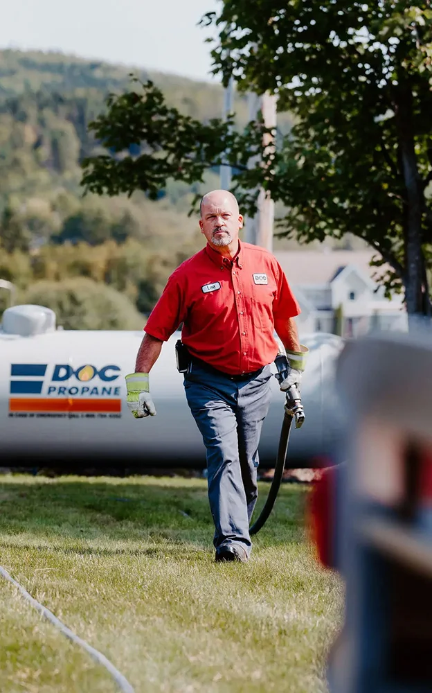 daigle employee walking the delivery hose back from a large propane tank across a lawn