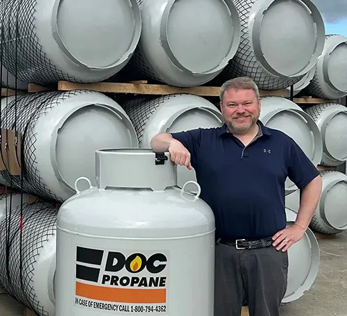 daigle employee leaning against a large propane tank with stacks of similar tanks behind him