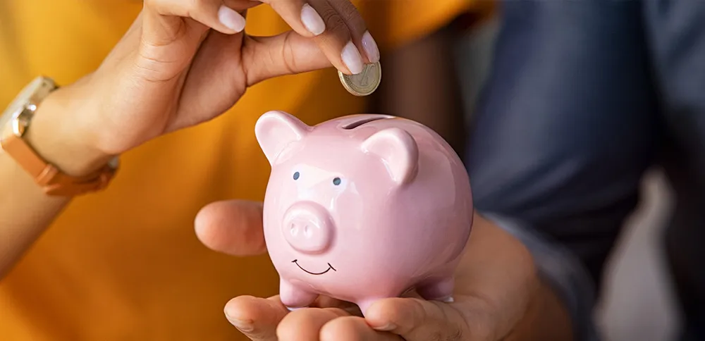 husband holds a small piggy bank while the wife puts a coin in
