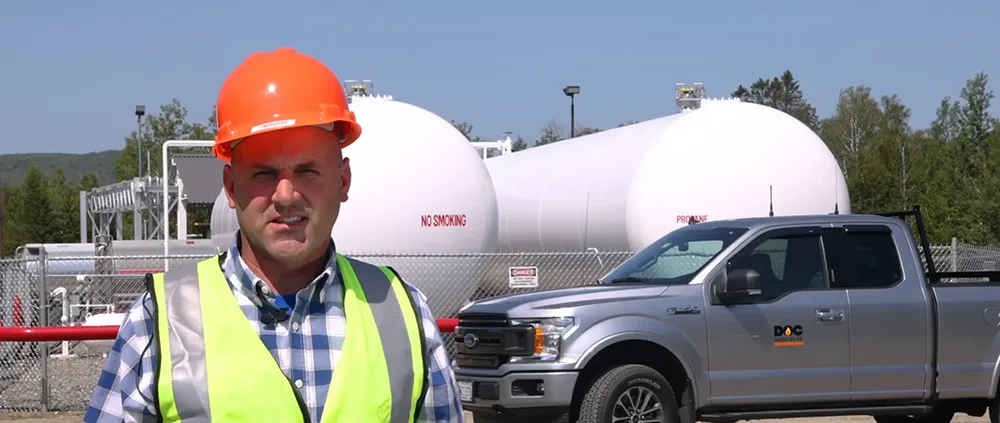 man standing in a hard hat and high-visibility vest in front of a daigle branded truck and propane tanks
